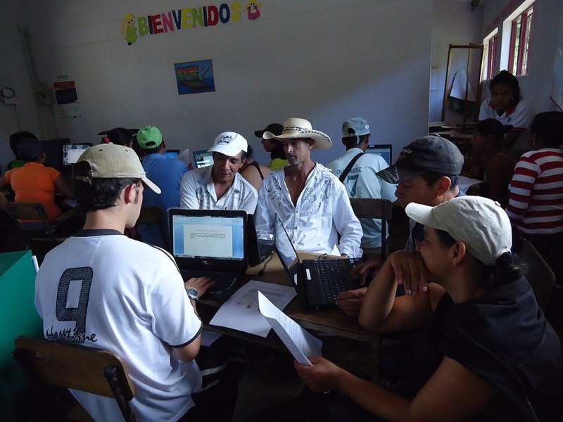Estudiantes de una vereda frente a computadores portátiles en un salón rural.